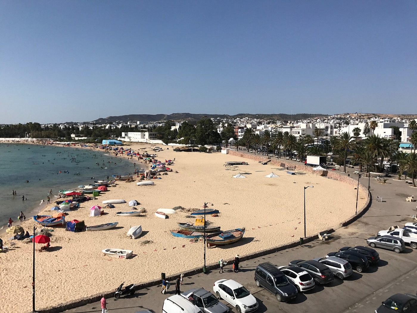 A calm, sandy beach at Hammamet, Tunisia, with swimmers in clear shallow water and the whitewashed town behind