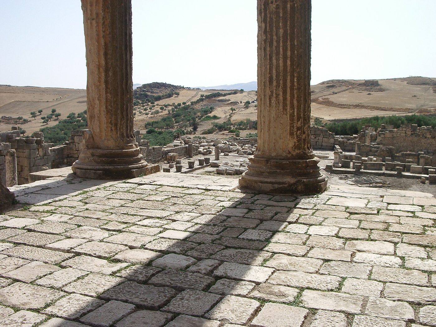 The Roman ruins of Dougga (Thugga), Tunisia — the Capitol temple and columns on the green hillside, showing spring greenery
