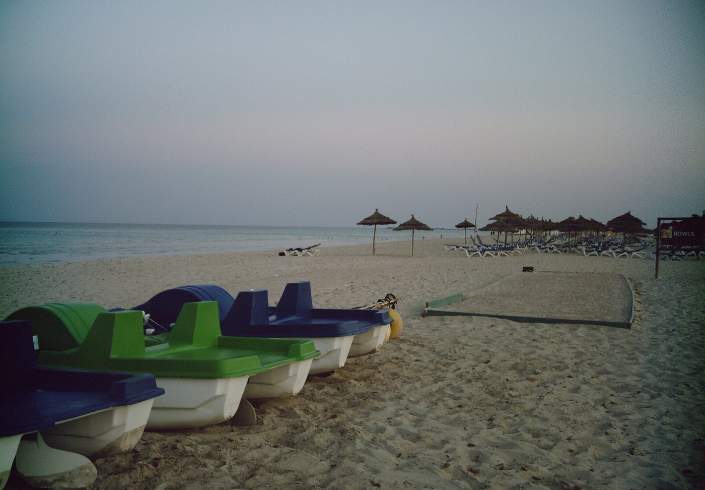 Pedalos and straw parasols on a Tunisian resort beach at dusk